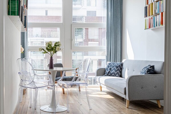 A modern living room with a grey sofa, clear chairs, a round table, and a vase of flowers.