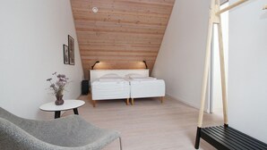 A modern bedroom with a sloped ceiling, a bed with white bedding, a small round table with a vase, and a grey armchair. - 2 bedroom beautiful apartment in Samsø (Samsø)