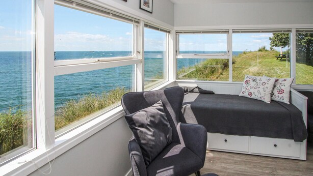 A bedroom with a large window overlooking the sea, a bed with floral pillows, and a chair. - Beautiful apartment in Samsø (Samsø)