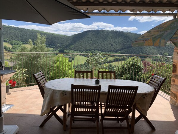 A round table with chairs on a balcony overlooking a mountainous landscape.