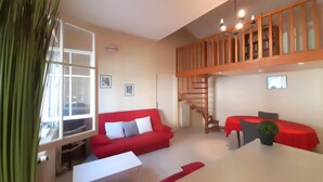 A modern living room with a red sofa, a white coffee table, a dining table with a red tablecloth, and a wooden staircase. - 2 bedroom beach front home in Cagnes-sur-mer (Cagnes-sur-mer)