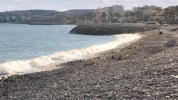 A rocky beach with waves crashing onto the shore, a stone wall, and buildings in the background. - 2 bedroom beach front home in Cagnes-sur-mer (Cagnes-sur-mer)
