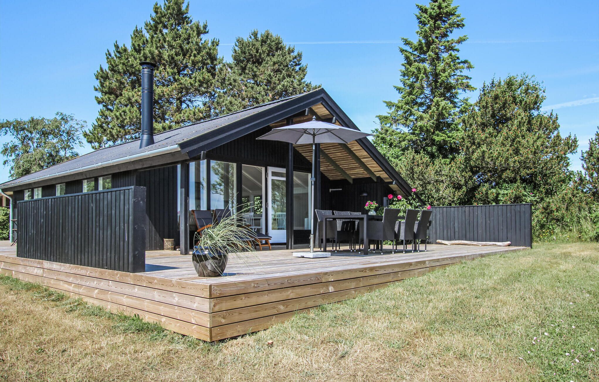 Una cabaña moderna con terraza, ventanas amplias y un espacio de estar al aire libre techado.
