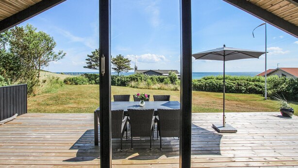 Terraza exterior con mesa y sillas, con vistas a una zona de césped y al mar.
