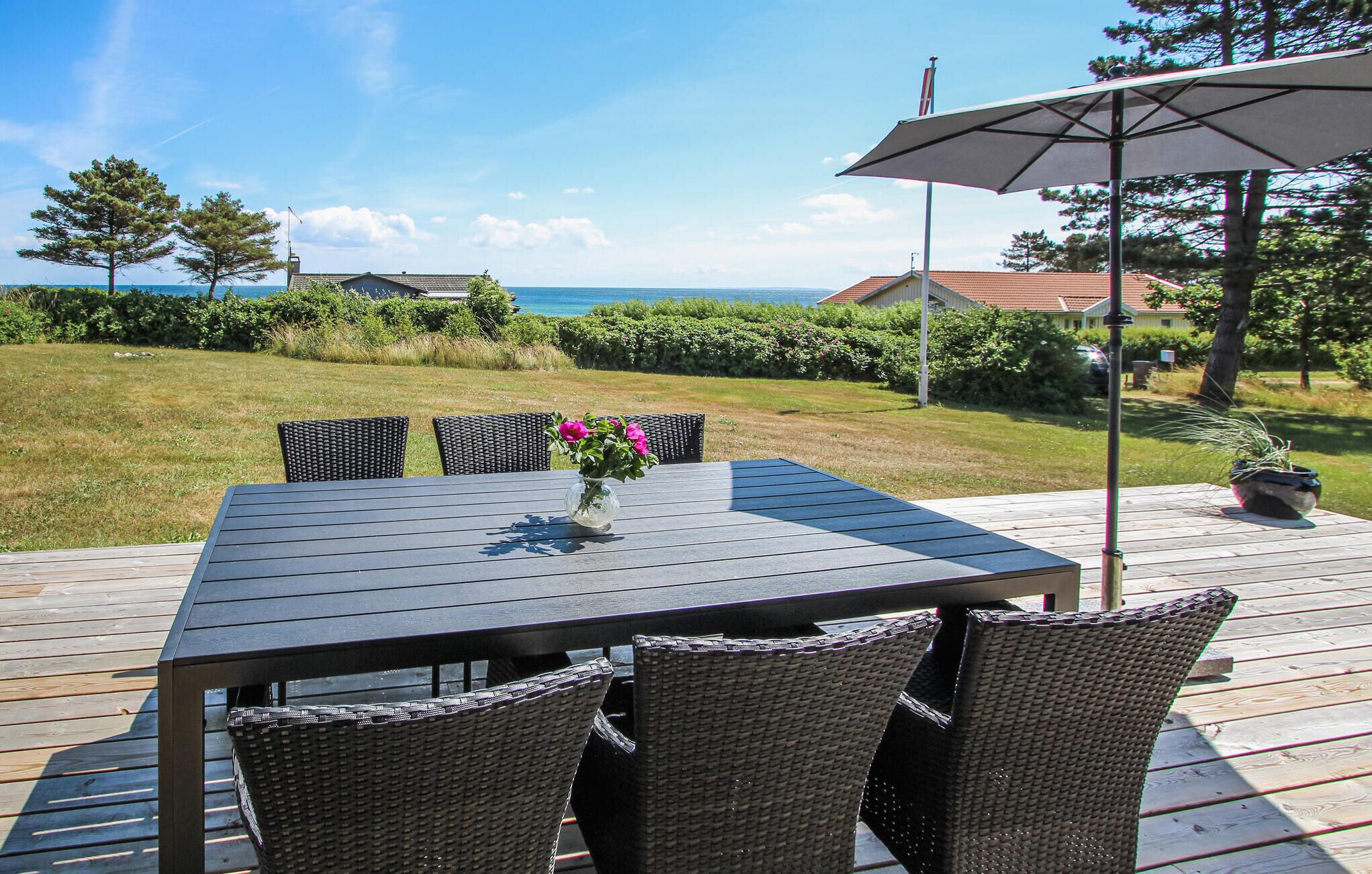 Une terrasse avec une table et des chaises, donnant sur une pelouse et un plan d’eau.