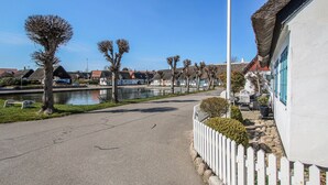 Un chemin pavé longe un plan d’eau, bordé de maisons traditionnelles et d’une clôture blanche en bois.
