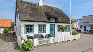 Une maison blanche avec un toit de chaume, des volets bleus et une clôture en bois peinte en blanc.