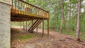 Eine Holzterrasse mit einer Treppe zu einem überdachten Bereich, umgeben von einem Wald.