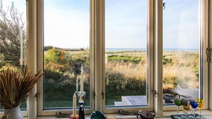 Ein Zimmer mit großem Fenster mit Blick auf eine Wiese und das Meer.