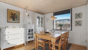A dining area with a wooden table and chairs, a white cabinet, and a window with a view of the outside. - Amazing home in Aabenraa (Aabenraa)