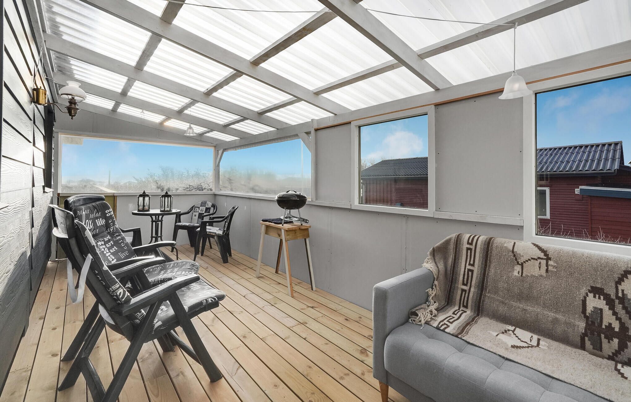 A covered patio with wooden flooring, a grey sofa, and a table with chairs.