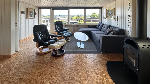 A modern living room with a black leather sofa, two black leather chairs, a white coffee table, and a wood-burning stove. - Amazing home in Aabenraa (Aabenraa)