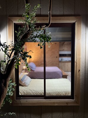 Una ventana con vista a una cama, almohadas y una mesita de noche.