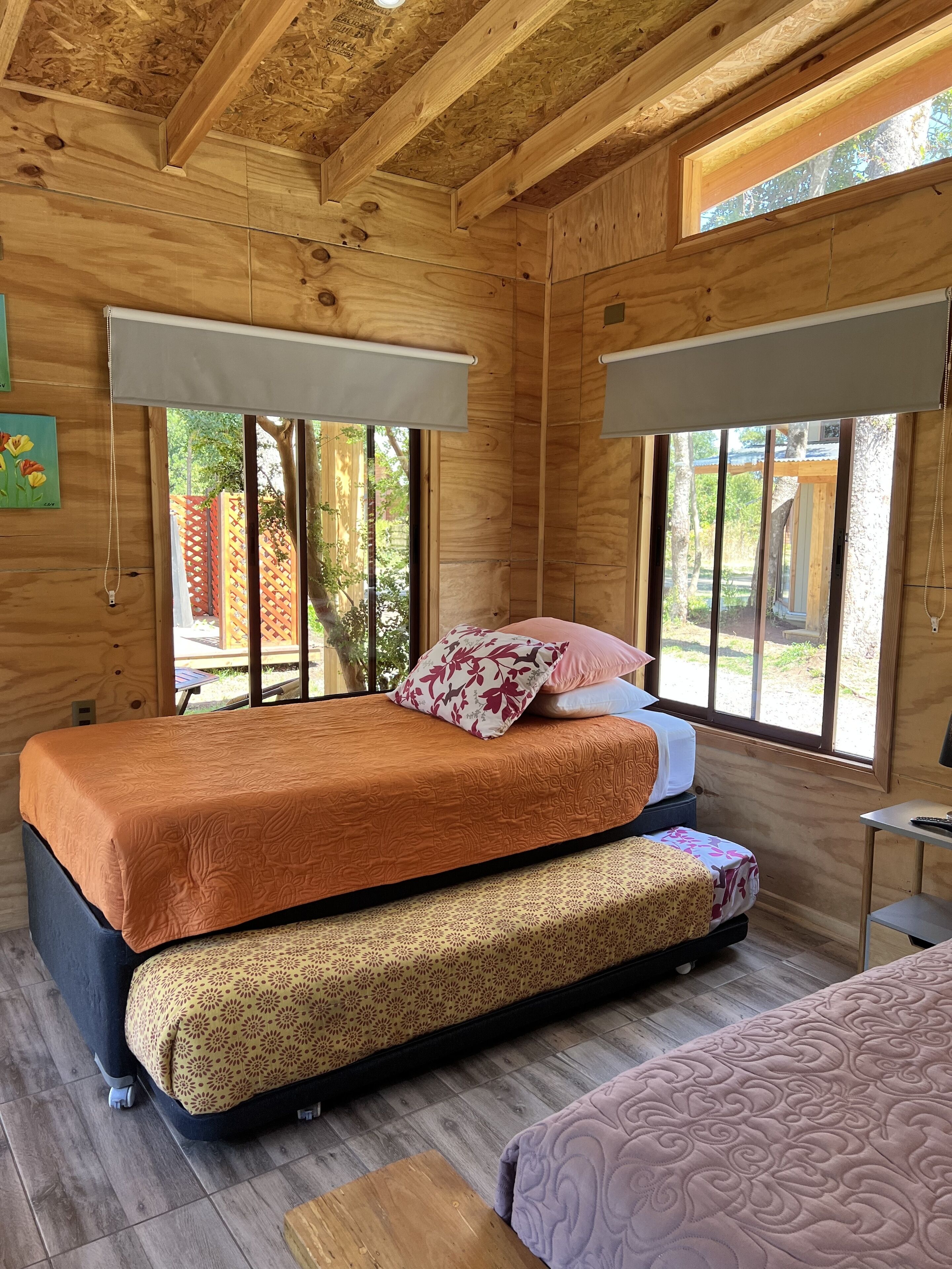 A wooden cabin bedroom with two beds, large windows, and a view of the outdoors.