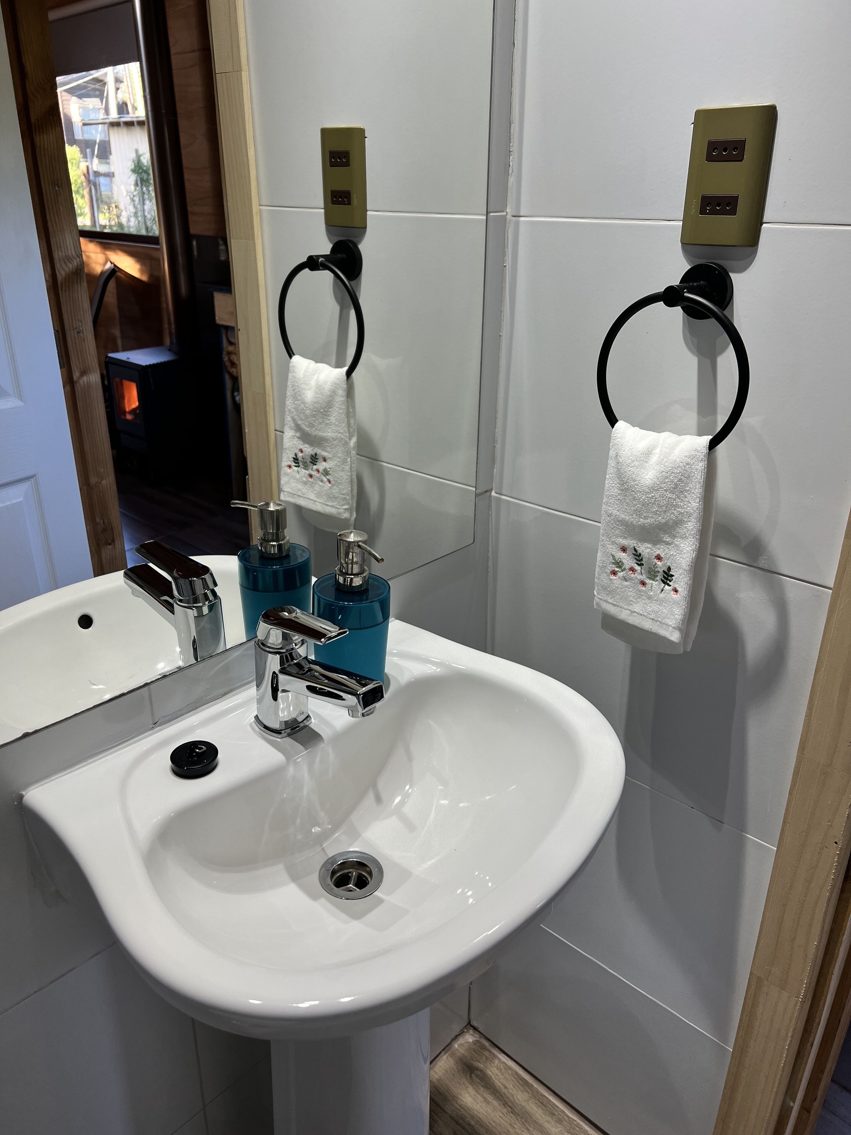 A bathroom with a white sink, chrome faucet, and towel rings with white towels.