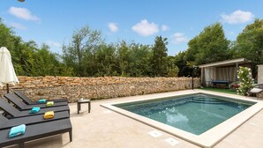 A swimming pool with lounge chairs and a stone wall.