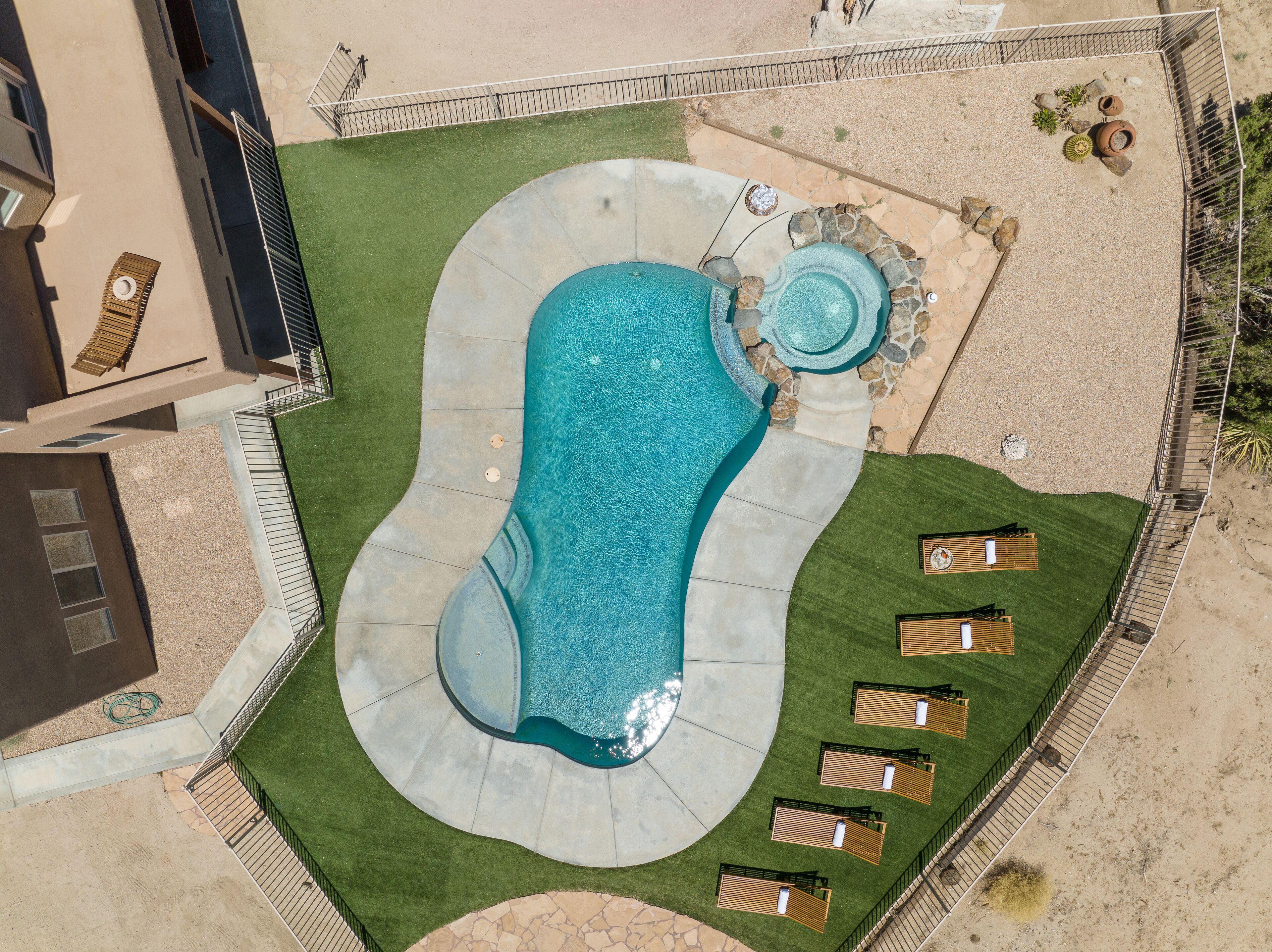 Vista aérea de una piscina con borde de piedra, rodeada de césped verde y tumbonas de madera.