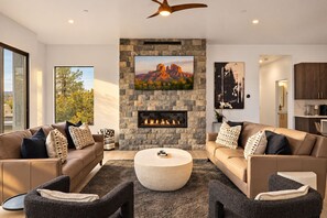 A modern living room with a stone fireplace, leather sofas, and a large flat-screen TV. - Sedona Epic Dream 5BR 2xPool w/Slide Rooftop Hottub / Sauna / Firepit (Sedona)