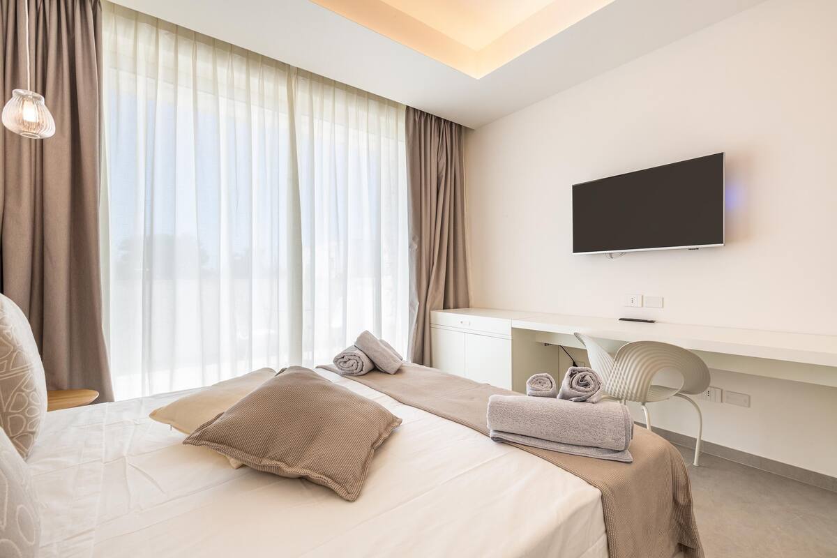 Ein modernes Hotelzimmer mit Bett, Schreibtisch, Stuhl und Fernseher.