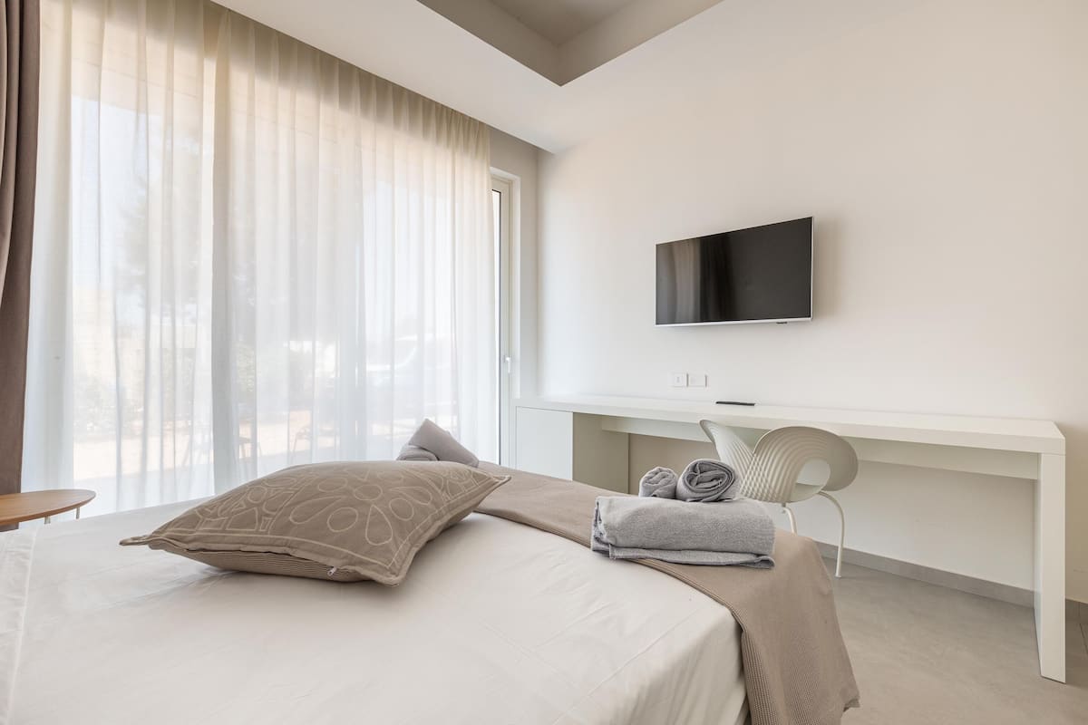 Ein modernes Hotelzimmer mit Bett, Schreibtisch, Stuhl und Fernseher.