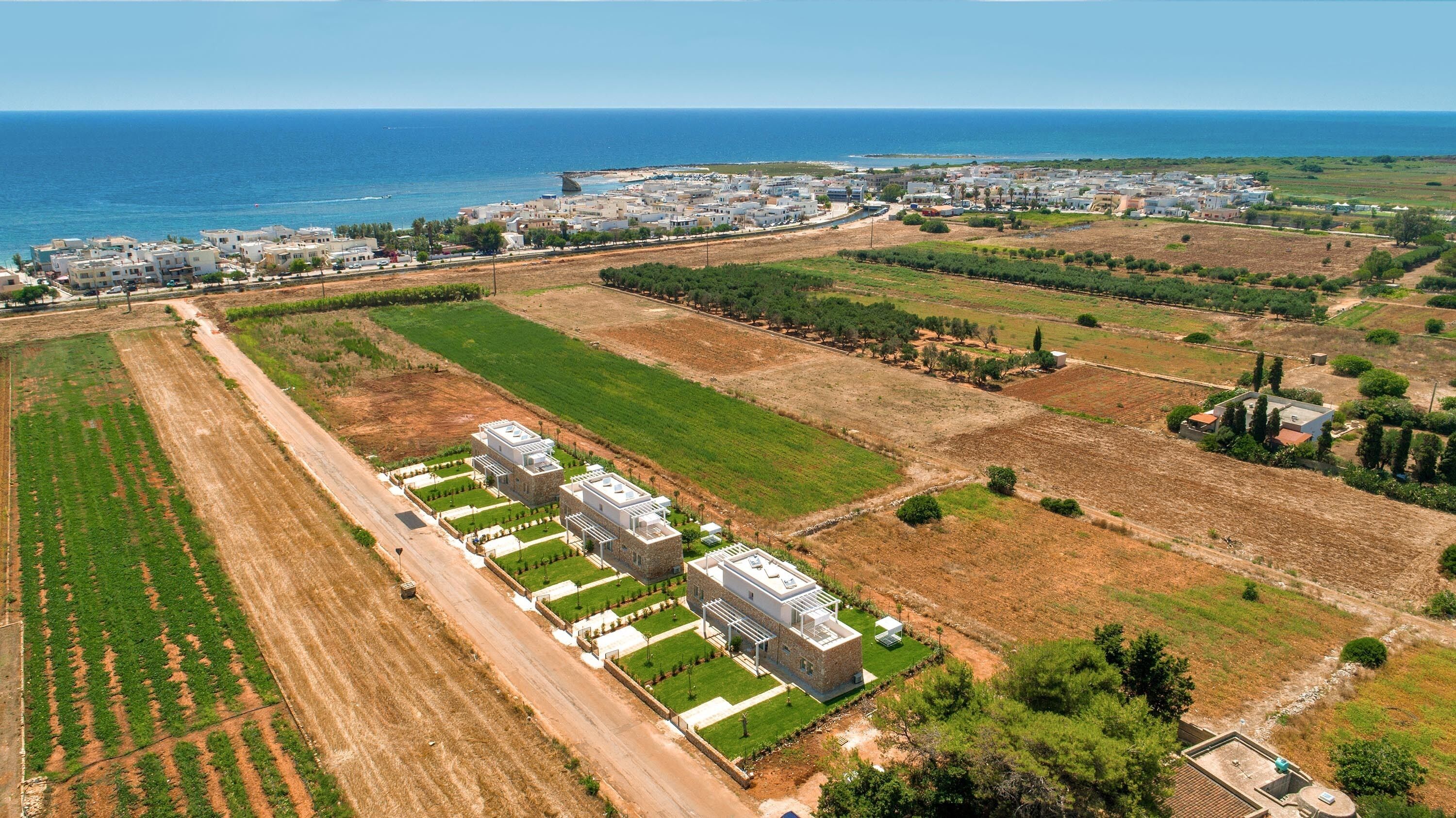 Une vue aérienne d’une zone côtière, avec un vaste complexe de bâtiments, des champs verdoyants et une vue dégagée sur la mer.