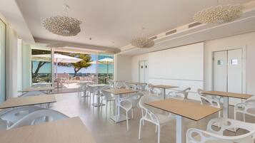 A modern classroom with white furniture and large windows overlooking a scenic view.