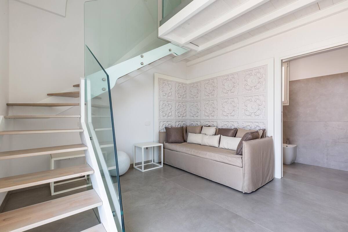 Ein modernes Interieur mit einer Glasstiege, einem beigen Sofa und einer Wand mit Muster.