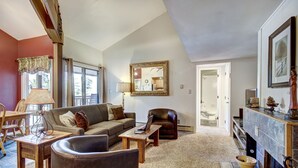 A living room with a sofa, a coffee table, a leather armchair, a fireplace, and a dining area with a table and chairs. - 2BR/2BA Condo on Shuttle Route - Wild Irishman 1015 - Pool & more! (Keystone)