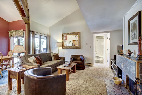 A living room with a sofa, a coffee table, a leather armchair, a fireplace, and a dining area with a table and chairs.