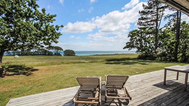 Een houten terras met twee stoelen gericht op een grasveld en uitzicht op de oceaan.