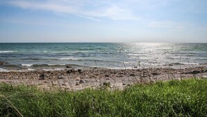 Een strand met kiezels en gras op de voorgrond, en de oceaan op de achtergrond.