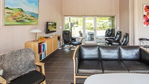 Een gezellige woonkamer met een bank, stoelen, een televisie en een boekenkast.