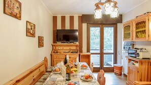 Un comedor con una mesa dispuesta para dos personas, un televisor sobre la encimera y una zona de cocina con armarios de madera y un radiador.