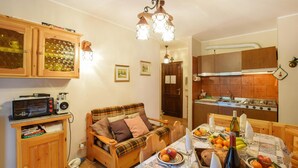 Una cocina acogedora con armarios de madera, una mesa de comedor dispuesta con frutas y una botella, y una kitchenette con estufa y fregadero.