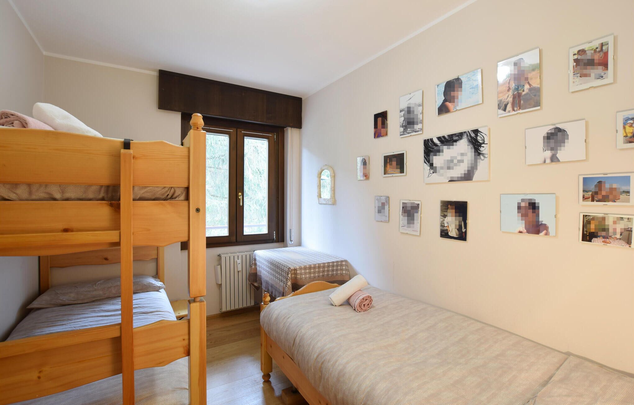 A bedroom with a bunk bed, a single bed, and a wall adorned with numerous photos.