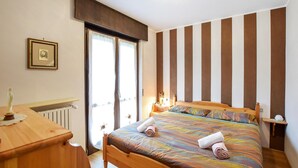 Un dormitorio con una cama, un aparador de madera, un radiador, un cuadro enmarco y una pared a rayas.