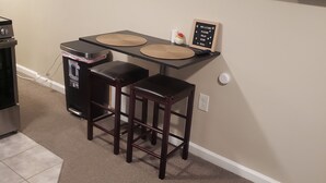 Een kleine keuken met een eettafel, twee krukken, een magnetron en een bordje 'Niet roken'.
