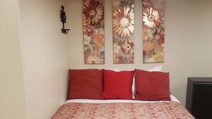 Een hotelkamer met een groot bed, rode en witte beddengoed, en twee bloemige kunstwerken aan de muur.