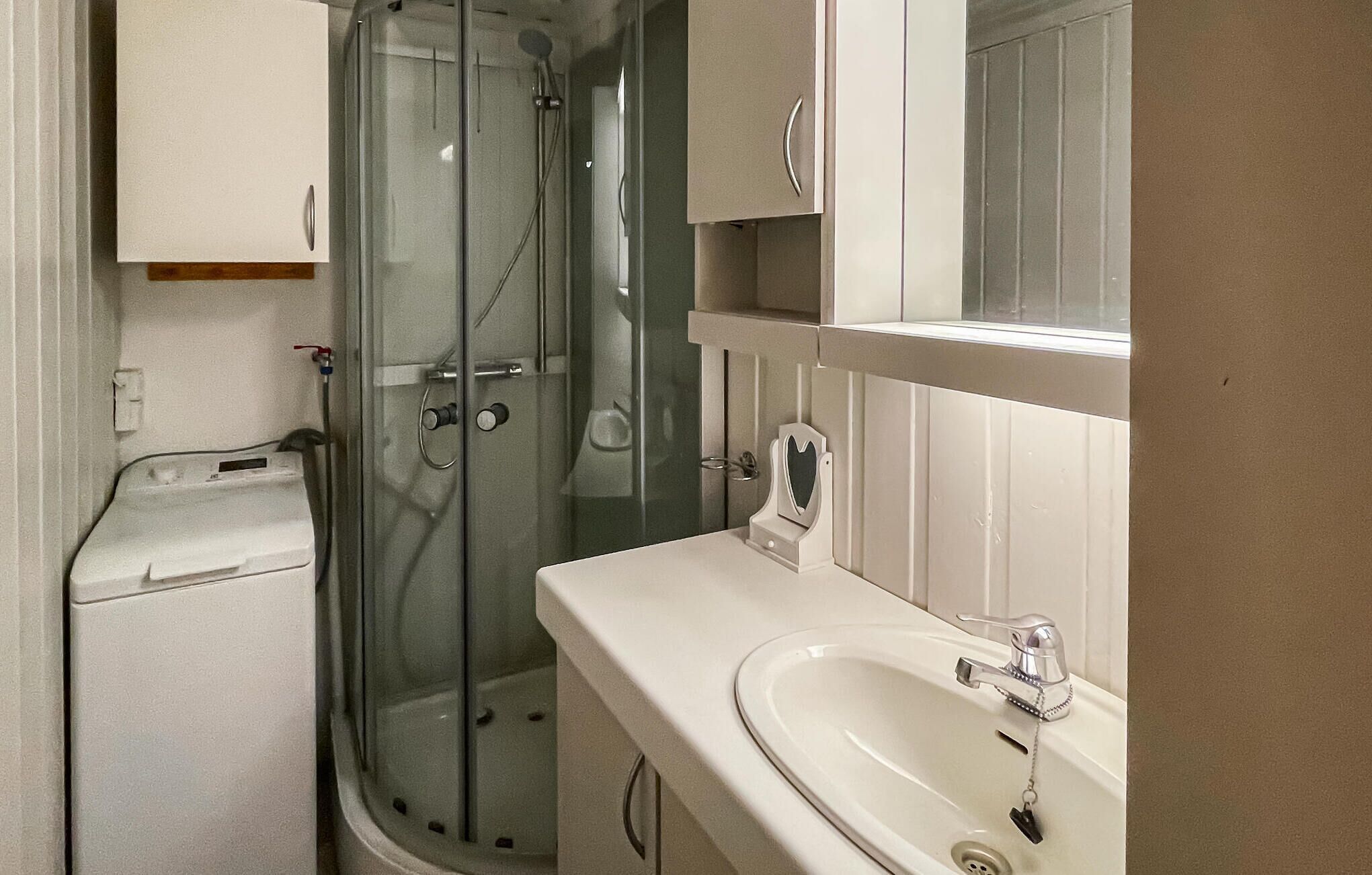 A bathroom with a glass shower enclosure, a white sink with a mirror above it, and a white cabinet.