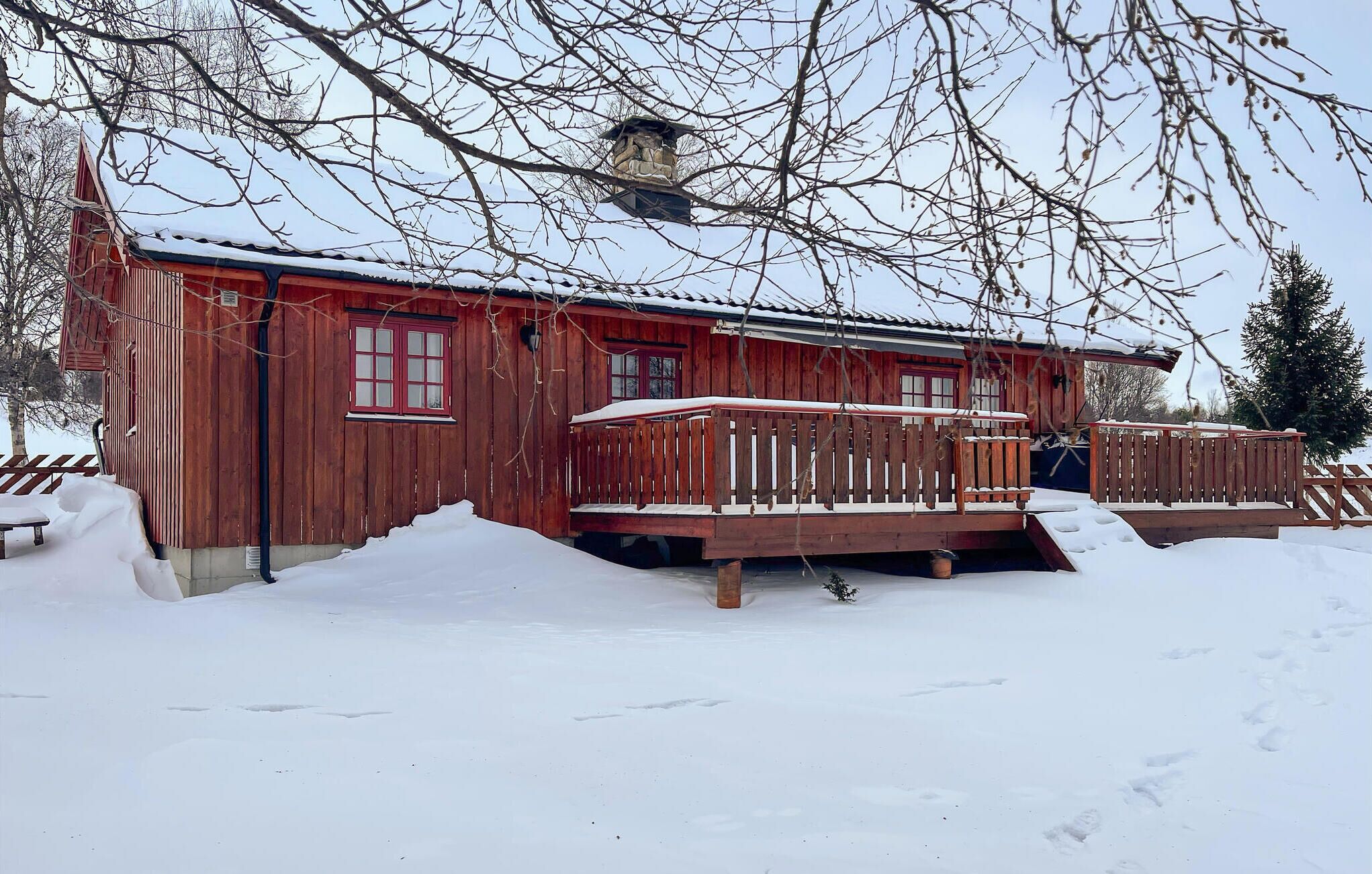En stuga av trä med röd fasad, en balkong och snö på marken.