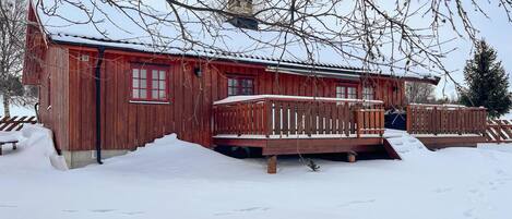 En stuga av trä med röd fasad, en balkong och snö på marken.