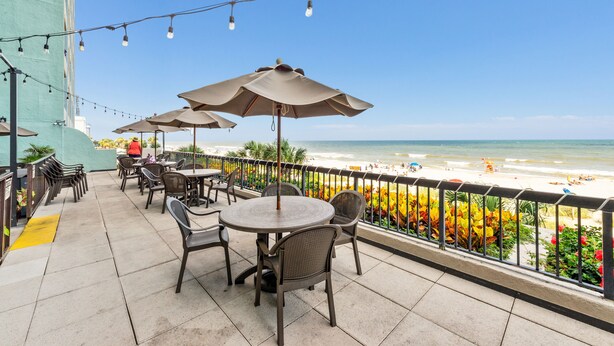 An outdoor patio with tables and chairs, overlooking a beach. - Beautiful Oceanfront Condo, breathtaking sunrises and a relaxing experience (Myrtle Beach)