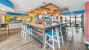 A bar area with a wooden ceiling, bar stools, and a counter with a television screen. - Beautiful Oceanfront Condo, breathtaking sunrises and a relaxing experience (Myrtle Beach)