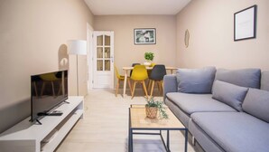 Uma sala de estar moderna com uma televisão de tela plana, um sofá cinza, uma mesinha de centro e um espaço de jantar com cadeiras amarelas.