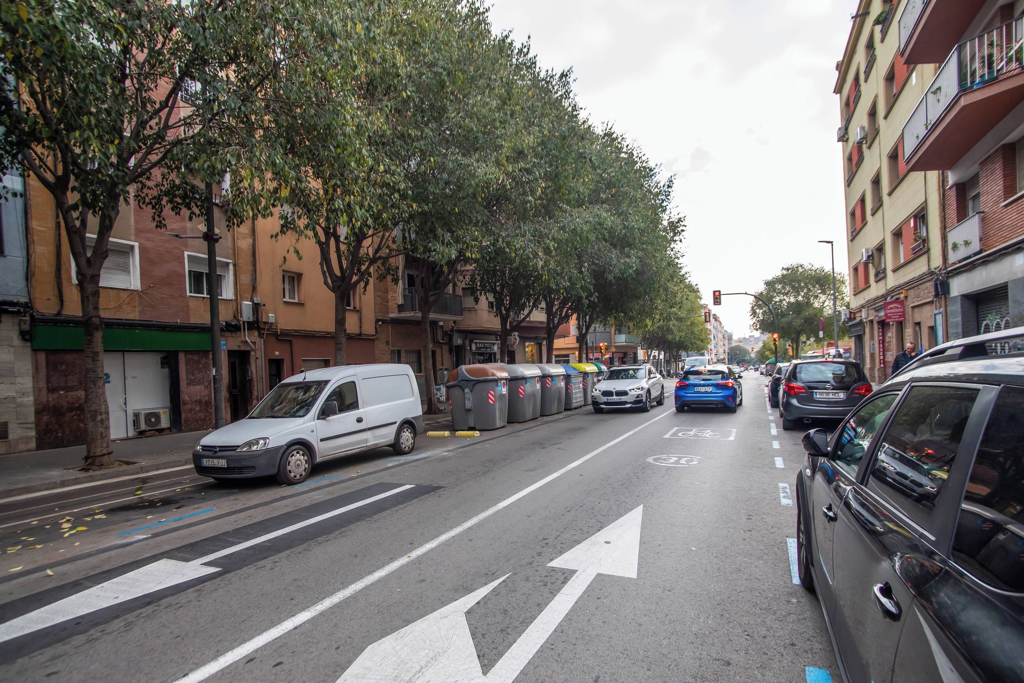 Calle bordeada de árboles y coches aparcados, con edificios a ambos lados.
