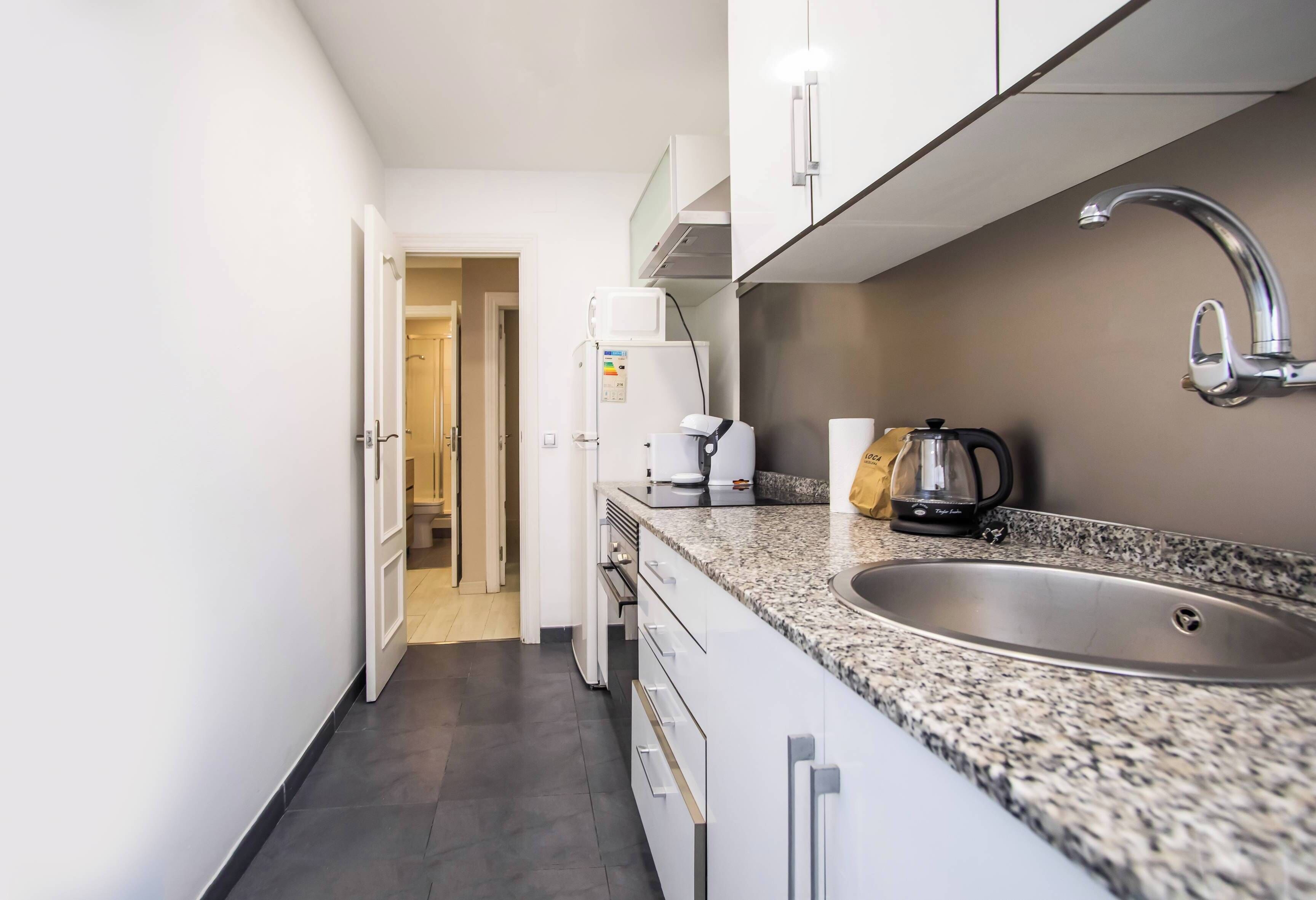 Una cocina moderna con armarios blancos, encimera de granito, pileta de acero inoxidable y cafetera.
