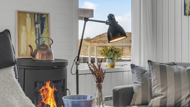 A cozy room with a fireplace, a table with a kettle, a lamp, and a view of a hill. - Awesome home in Pandrup with WiFi (Pandrup)
