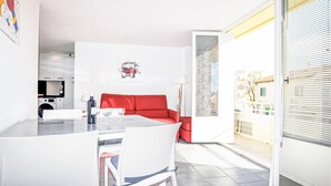 A modern living room with a red sofa, a dining area with a table and chairs, and a kitchen in the background. - Stunning apartment in Saint Cyprien Plage (Saint Cyprien Plage)