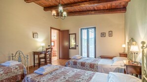 Un dormitorio con dos camas, techo de madera, un escritorio con silla y una puerta que da a otra habitación.
