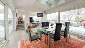 Ett modernt matområde med ett glasbord och stolar, en mönstrad matta och utsikt över en snötäckt trädgård genom stora fönster.
